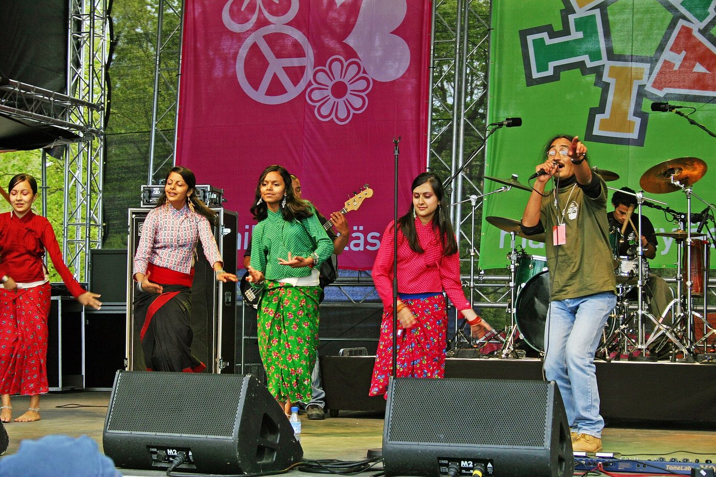 Amrit Gurung von Nepathya singt auf einer Festivalbühne im Freien, neben ihm vier Tänzer in Rot und Grün