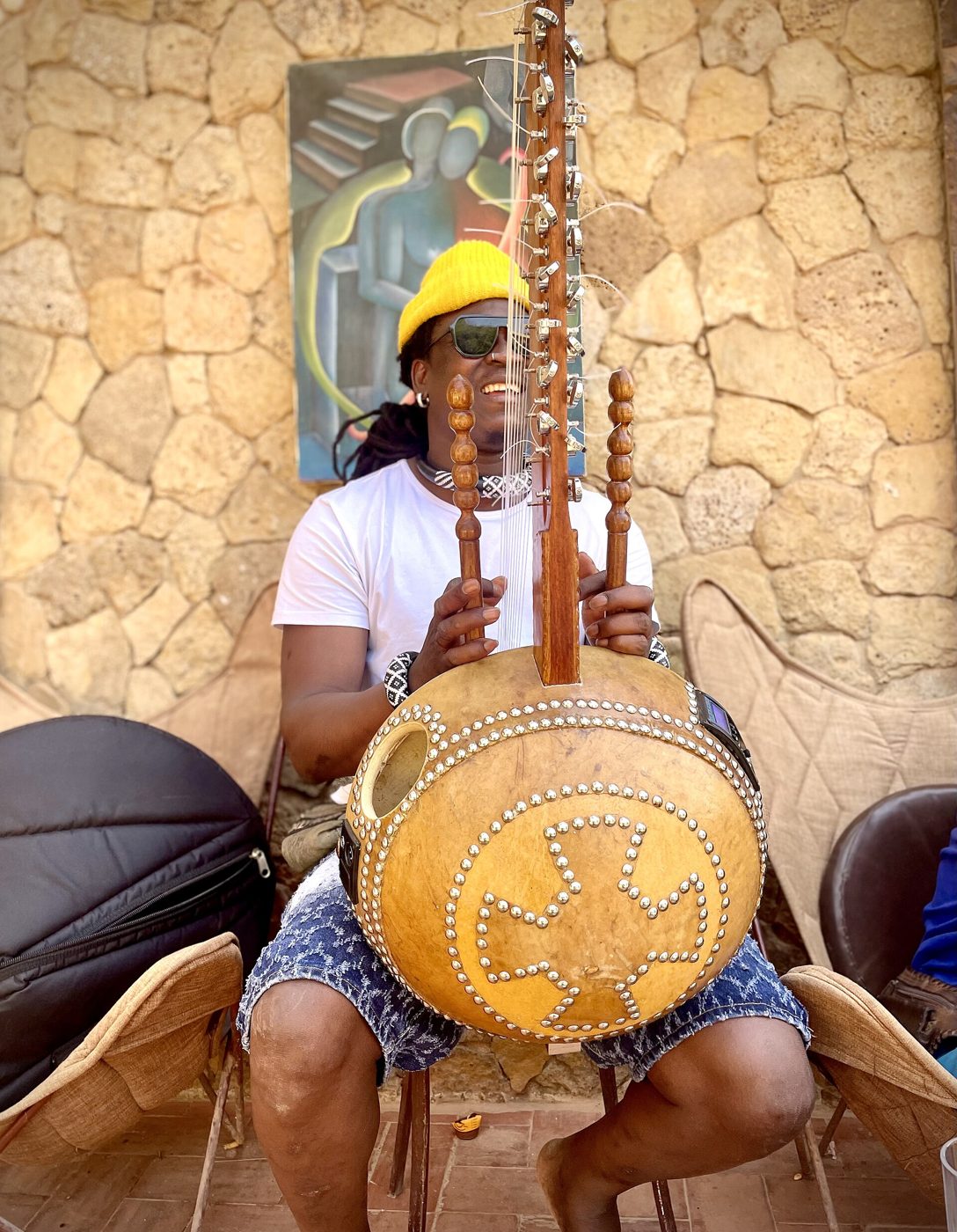 Ein lächelnder Koraspieler sitzt mit seinem Instrument vor einer Steinmauer